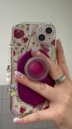 a woman's hand holding a phone case with flowers on it and a pink ring