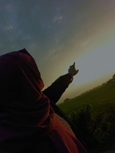 a person wearing a purple shawl and holding their hands up in the air while standing on top of a lush green field