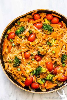 a skillet filled with noodles, broccoli and tomatoes