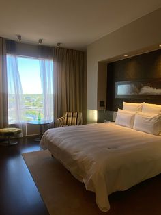 a large white bed sitting in a bedroom next to a window with curtains on it