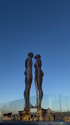 two metal statues standing next to each other in front of a blue sky with clouds