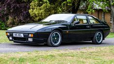 a black sports car parked on the side of a road next to trees and grass