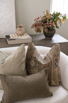 three pillows on a white chair in front of a vase with flowers and other decorative items