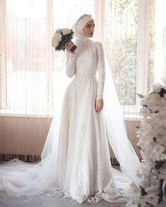 a woman in a white wedding dress standing next to a window with flowers on it