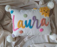 a white pillow with the word laurie written on it and pom poms in front