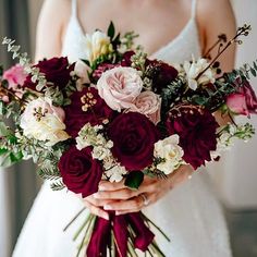 a bride holding a bouquet of red and white flowers with greenery in her hands