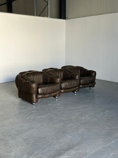 two brown leather couches sitting next to each other in an empty room with white walls