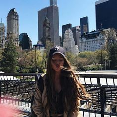 a woman sitting on top of a bench in front of a large cityscape