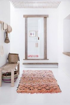 a white room with a bench and rug on the floor, next to a door