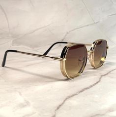 These aviator sunglasses feature a vintage 70s-inspired design with an octagonal shape. The lenses have a stylish brown ombre tint, perfectly complemented by a sleek gold metal frame. Suitable for both men and women, these shades add a retro flair to any look while offering classic pilot style. NOS Deadstock Made in Europe FIT INFORMATION  55mm Eye Size 22mm Bridge 145mm Temple/Arm Width 5 Inches Height 1 3/4 Inches Luxury Elegant Men's Aviator Sunglasses, Tan Luxury Sunglasses, Luxury Gold Aviator Sunglasses With Metal Frame, Luxury Vintage Gold Aviator Sunglasses, Retro Aviator Sunglasses With Uv Protection And Square Frame, Retro Square Frame Aviator Sunglasses With Uv Protection, Retro Aviator Sunglasses With Metal Frame, Retro Brown Shield Sunglasses With Square Frame, Retro Brown Square Frame Shield Sunglasses