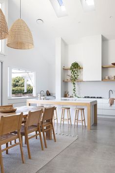 an open kitchen and dining room area with white walls, wooden furniture and hanging lights