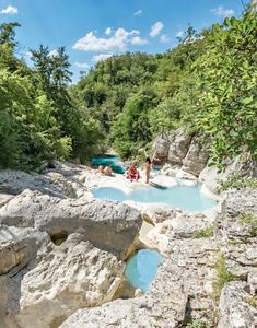 two people are sitting on the rocks near a pool in the middle of a forest