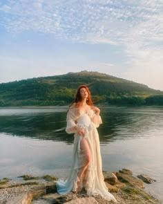 a woman in a white dress standing on rocks near water