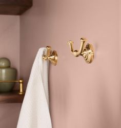 a bathroom with pink walls and gold fixtures on the towel rack, toilet paper roll and soap dispenser