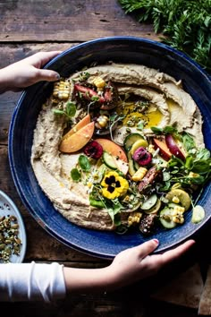 a person holding a blue plate with hummus and vegetables on it next to other dishes