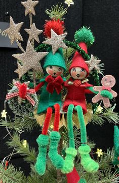 an ornament on top of a christmas tree with two elfs hanging from it