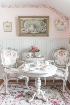 a white table and chairs in a room with pink flowers on the wall behind it