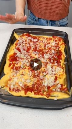 a woman standing in front of a pizza on a pan with cheese and tomato sauce