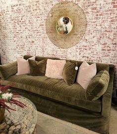 a living room with brick walls and green velvet couches in front of a round mirror