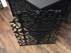 a black table with an intricate design on it's top and bottom, sitting on a wooden floor