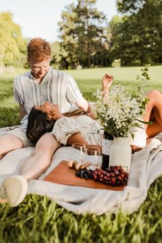 a man and woman sitting on top of a blanket in the grass