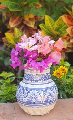 a blue and white vase with purple flowers in it sitting on a table next to some plants