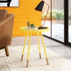 a yellow table with a plant on it in front of a brick wall and brown leather chair