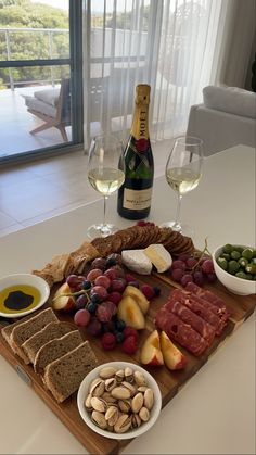 a wooden tray topped with lots of food and wine next to two glasses of wine