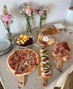 a table topped with different types of pizzas and appetizers next to vases filled with flowers