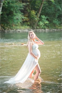 a pregnant woman is standing in the water wearing a white dress and posing for a photo