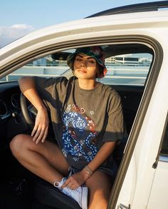 a young woman sitting in the passenger seat of a car wearing a hat and sunglasses