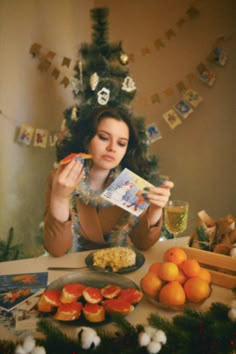 a woman sitting in front of a christmas tree holding up a piece of paper next to an orange