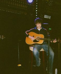 a man sitting in front of a microphone while playing an acoustic guitar at a concert