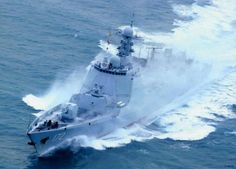 an aerial view of a navy ship sailing in the ocean with spray coming from it