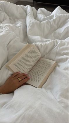 a woman laying in bed reading a book with her hand on top of an open book