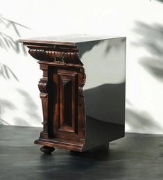 an old wooden clock sitting on top of a table next to a planter and wall