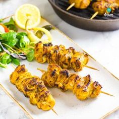 several skewers of chicken are on a plate with salad and lemon wedges