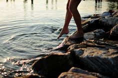 a person standing on rocks in the water with their feet in the water and one foot sticking out of the water