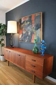 a living room with a large painting on the wall next to a wooden dresser and lamp