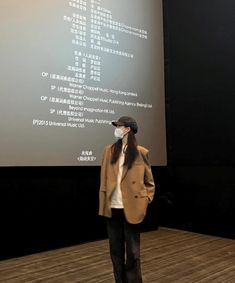 a woman standing in front of a projection screen wearing a face mask and looking at it