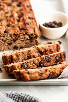 sliced loaf of chocolate chip banana bread on a white plate with two bowls of chocolate chips