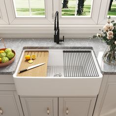 a white kitchen sink sitting under a window next to a cutting board and bowl of fruit