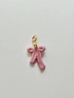 a small pink teddy bear charm hanging from a gold plated metal hook on a white surface