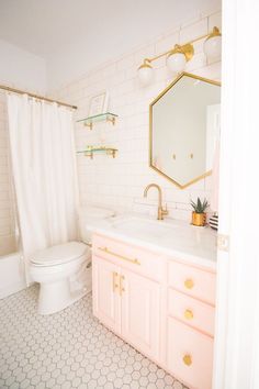 a bathroom with white tile and pink vanity, gold hardware on the faucet