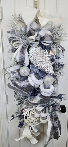 a wreath with silver and white decorations hanging on the front door, decorated with ribbons