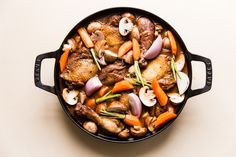 a skillet filled with meat and vegetables on top of a white table next to a spoon