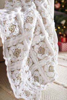 a white crocheted blanket sitting on top of a couch next to a christmas tree