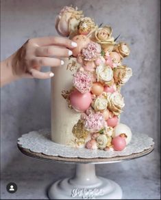 a woman's hand on top of a white cake with pink and yellow flowers