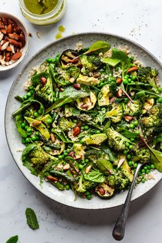 a white plate topped with broccoli and peas next to two bowls of nuts