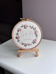 a white table with a wooden stand holding a cross - stitch embroidered monogram on it